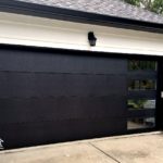 Modern black garage door against a white garage with windows on the right side of the garage door showing a modern design